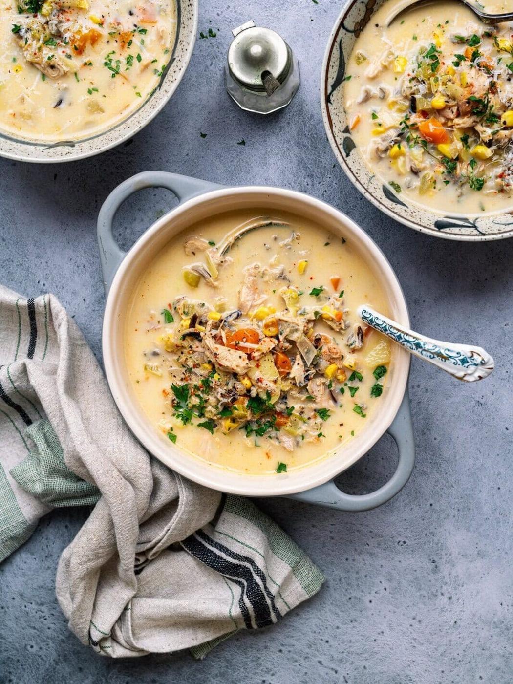 Crockpot turkey soup in a small ceramic pot, two bowl servings partially seen on the side