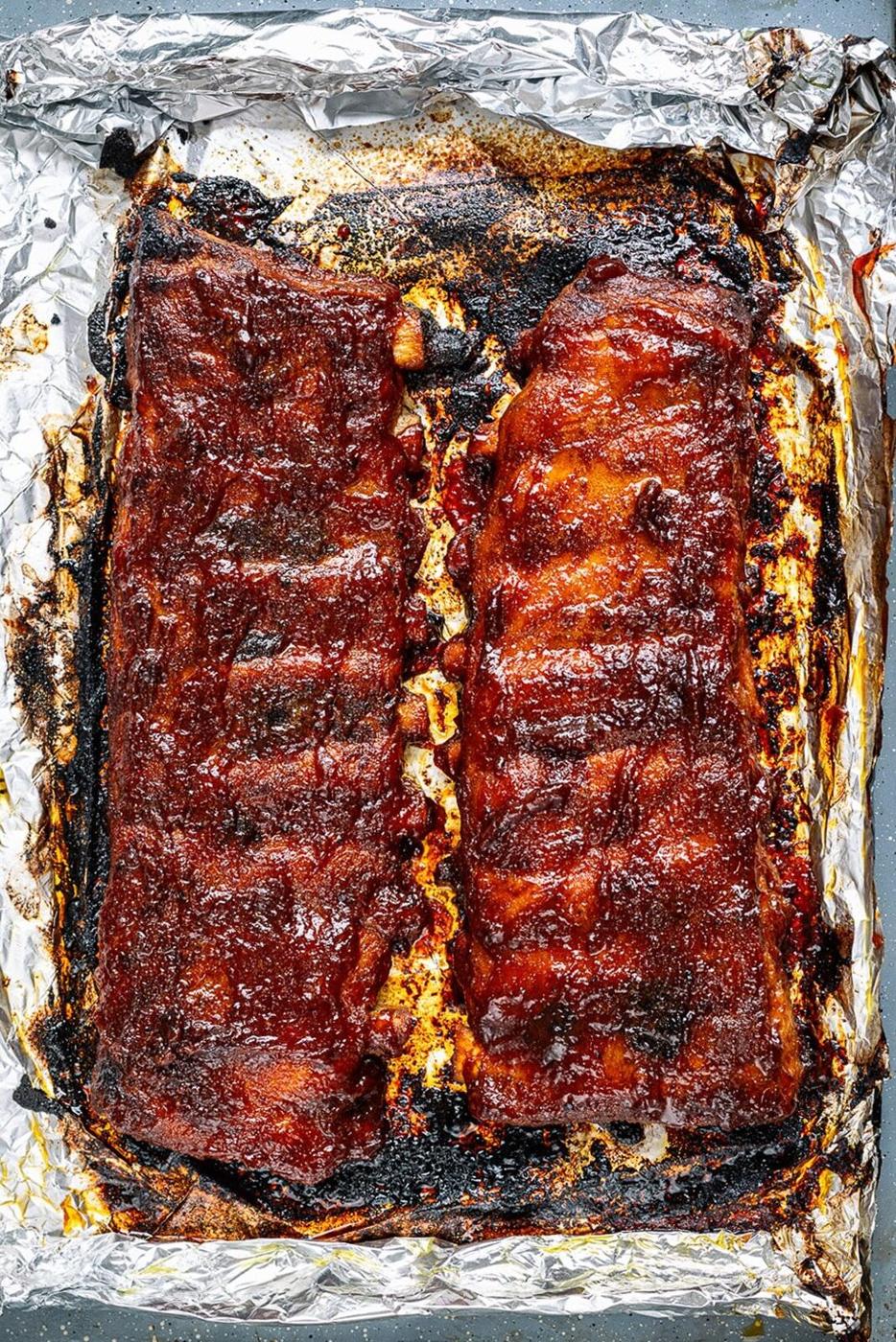 two racks of oven baked barbecue ribs on a foil lined baking tray