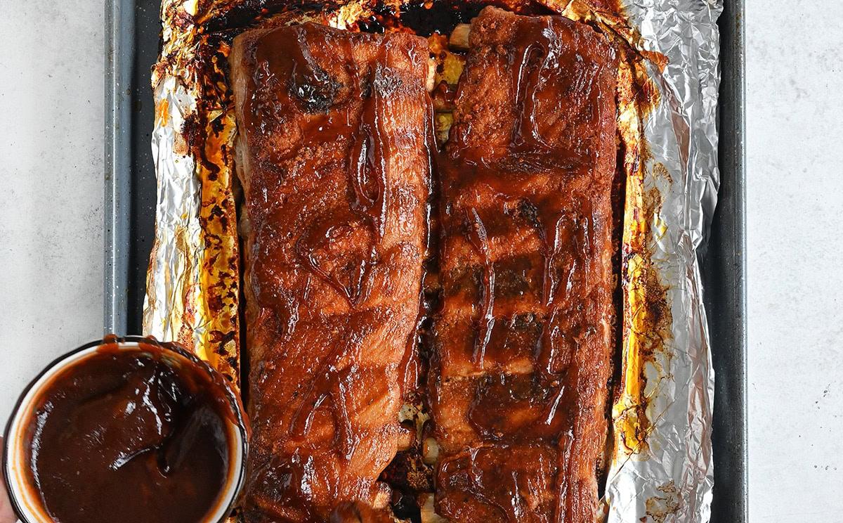 brushing oven baked pork ribs with barbecue sauce