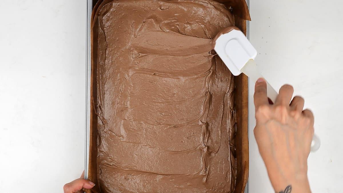 spreading chocolate cake batter into a rectangular baking tin