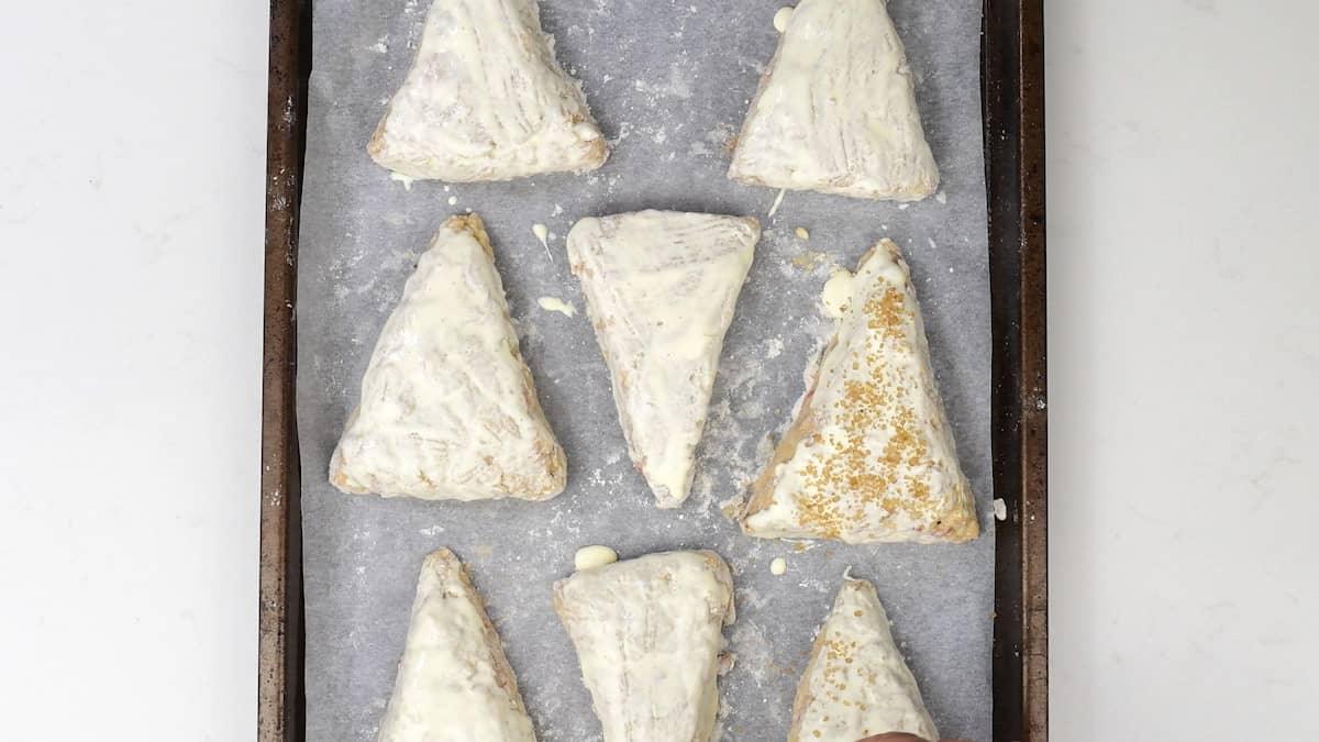 brushing apple scones with cream and sprinkling with sugar