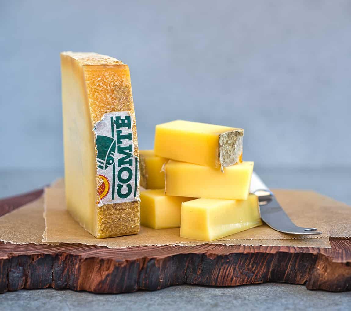 Slice of Comte cheese on a wooden board with cubed cheese on the side