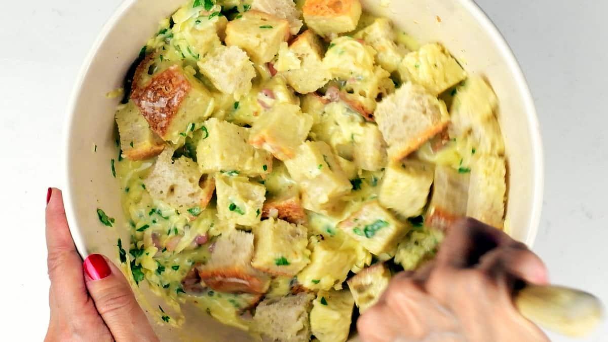 mixing bread cubes with eggs, milk and cheese in a bowl