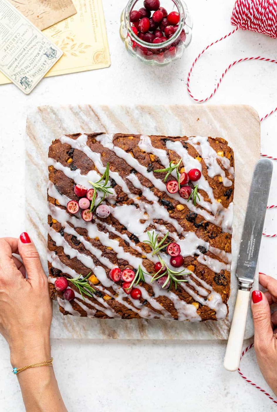 Square slimming world fruitcake drizzled with glaze and decorated with rosemary sprigs and chopped cranberries