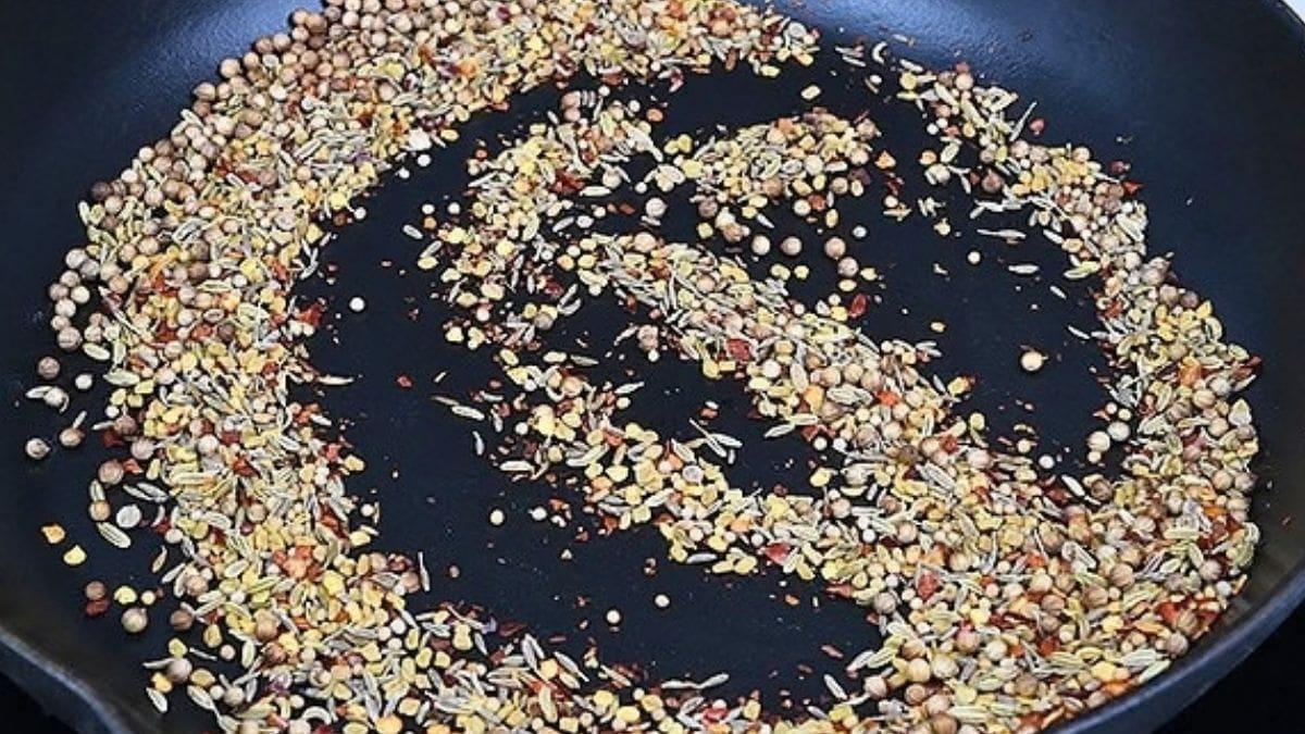 Whole coriander, fennel and mustard seeds dry-toasting in a black skillet for the lamb bhuna spice blend.