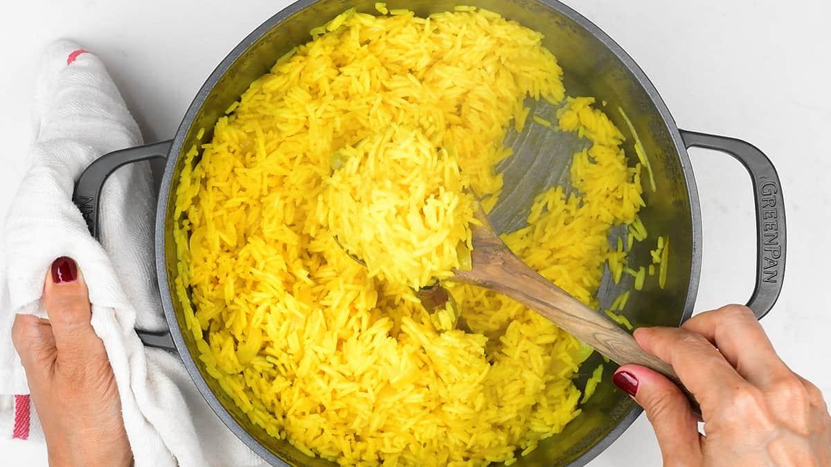 Stirring pilau rice in a pot with a wooden spoon