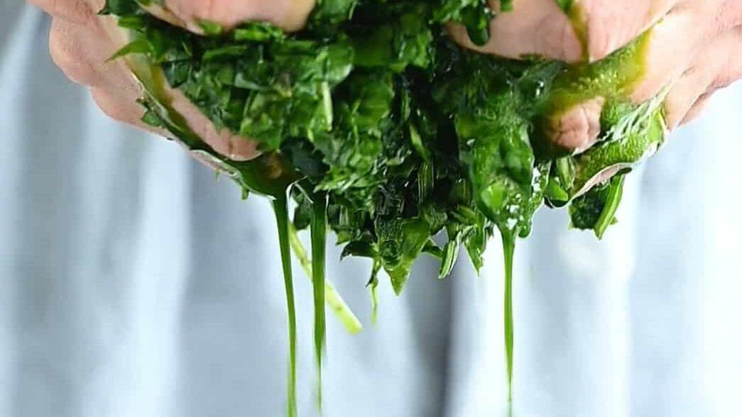 squeezing chopped spinach over a bowl to get rid of liquid