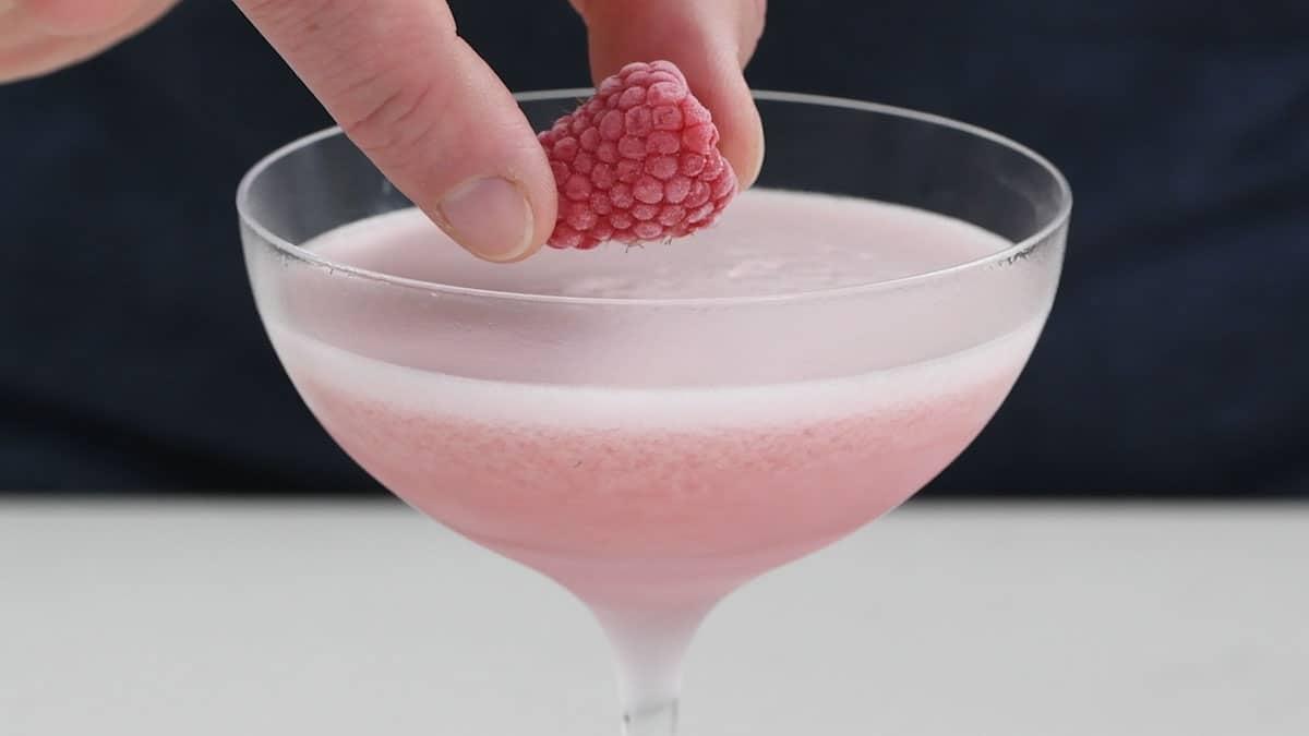 Frothy French Martini being garnished with a raspberry