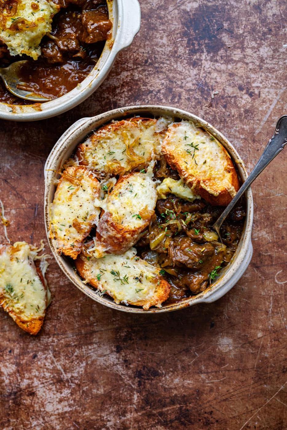 French onion beef stew topped with cheesy bread slices in an ovenproof bowl.