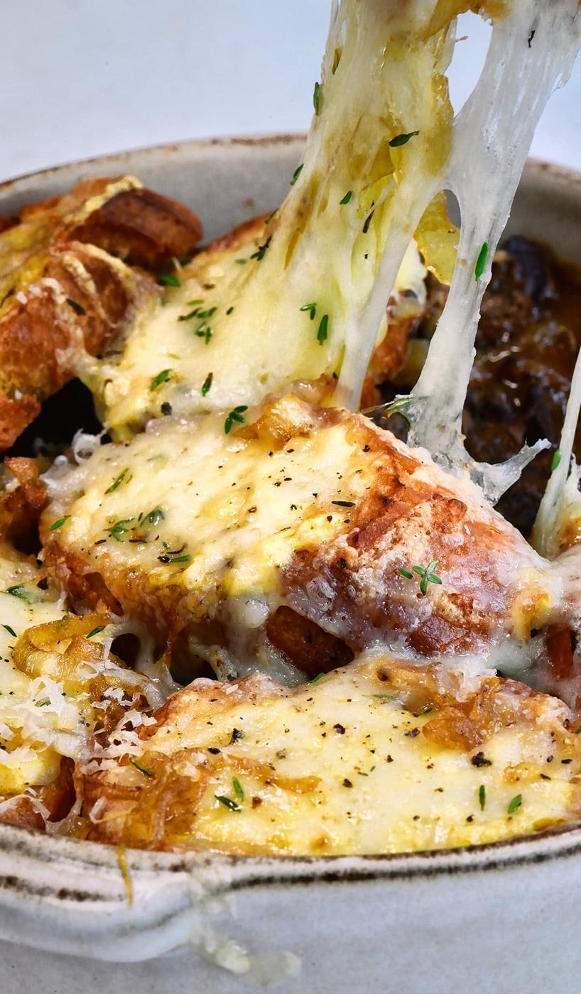 Pulling a cheesy bread slice off the top of a bowl of French onion beef stew