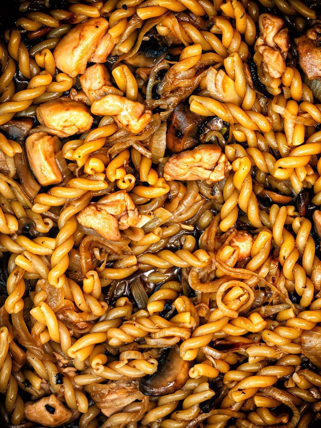 Close-up of cooked gemelli pasta mixed with chicken, sautéed onions, and mushrooms, all coated in a rich brown sauce. This one pot French Onion Pasta dish looks flavorful and savory, with ingredients evenly distributed for a hearty meal.