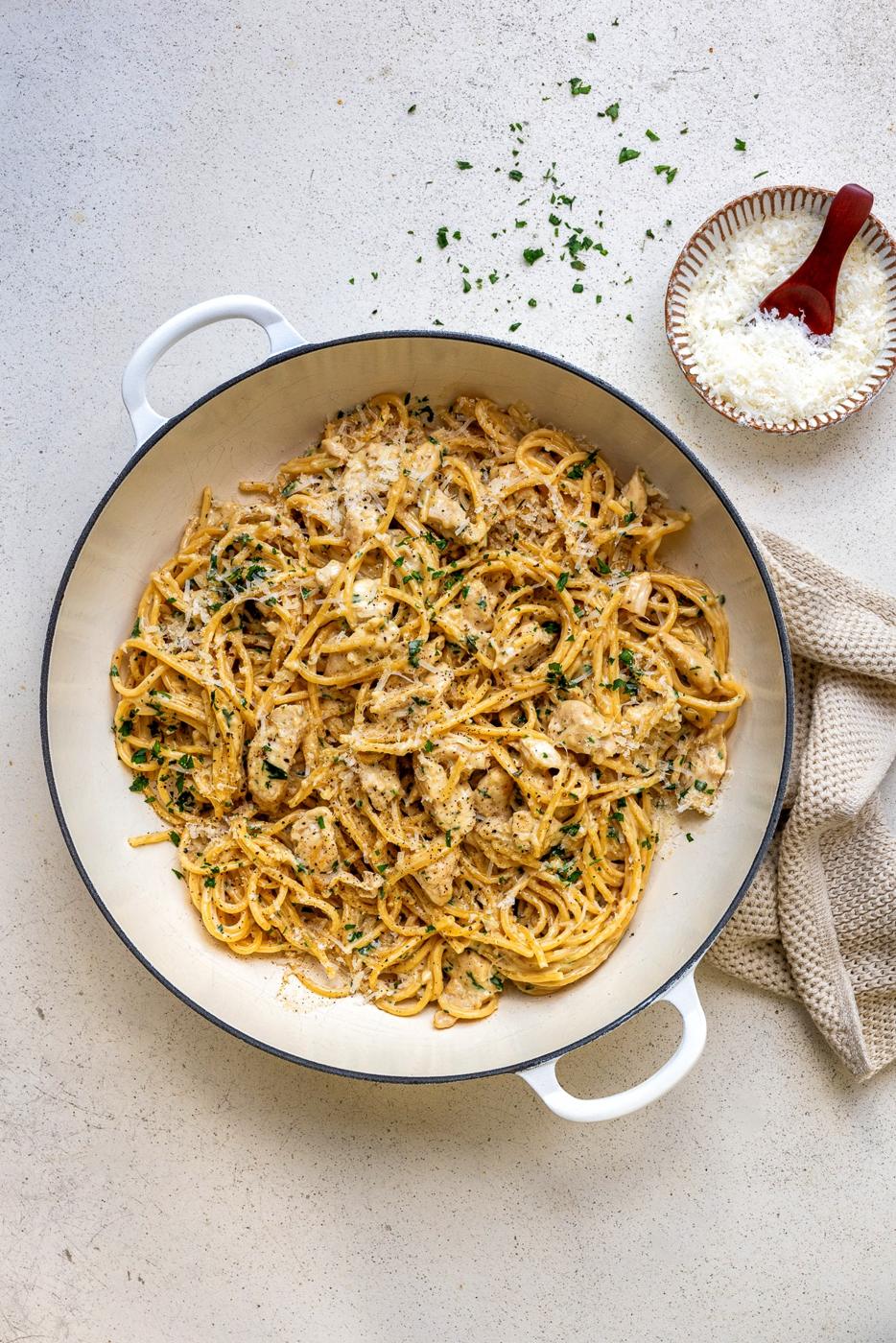 overheat view of a pan of Garlic parmesan chicken with spaghetti, bowl of grated Parmesan on the side