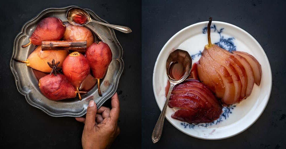 A hand holds a metal platter with poached pears, a cinnamon stick, and a spoon. Beside it, a white plate with two poached pear halves and a spoon rests on a dark surface, perfect alongside a slice of ginger layer cake.