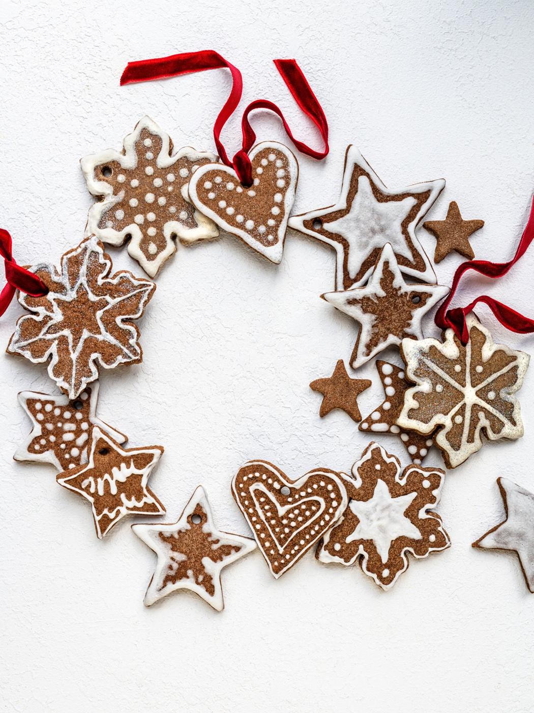 A wreath made of decorated gingerbread salt dough ornaments shaped like stars, hearts, and snowflakes, all tied together with red ribbons, arranged on a white background.