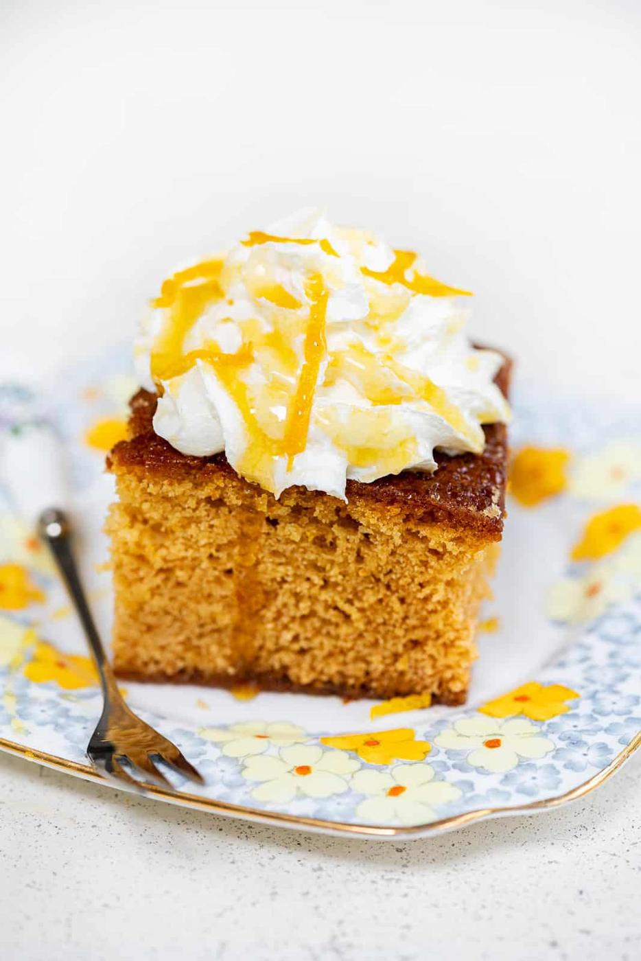 Golden syrup cake topped with whipped cream on a floral plate