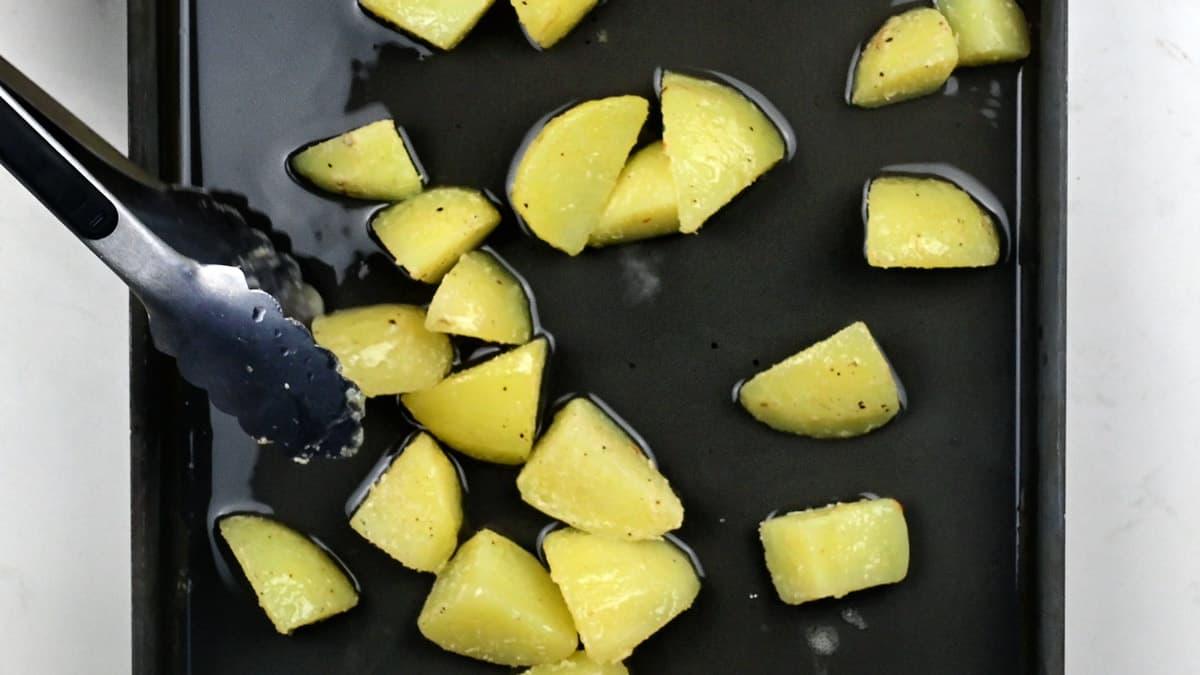 Adding parboiled potatoes to roasting tray with hot goose fat