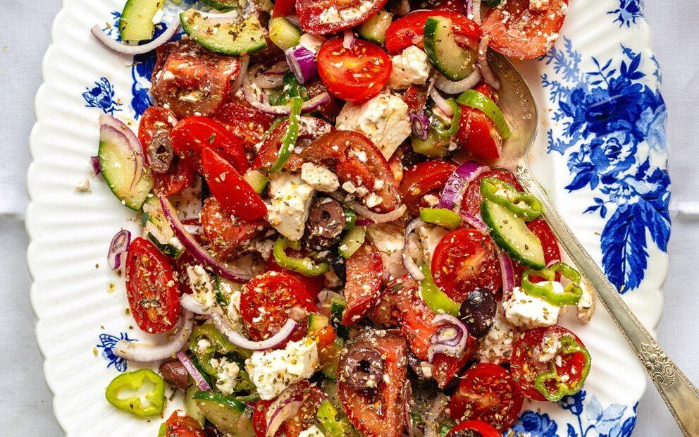Greek salad on a blue and white floral platter with tzatziki sauce and grilled chicken on the side