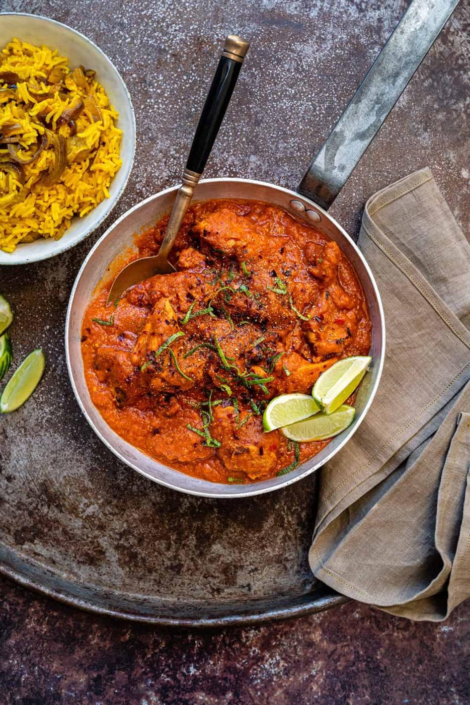 Slimming World Chicken Tikka Masala in a pan with lime wedges on the side and lime zest garnish