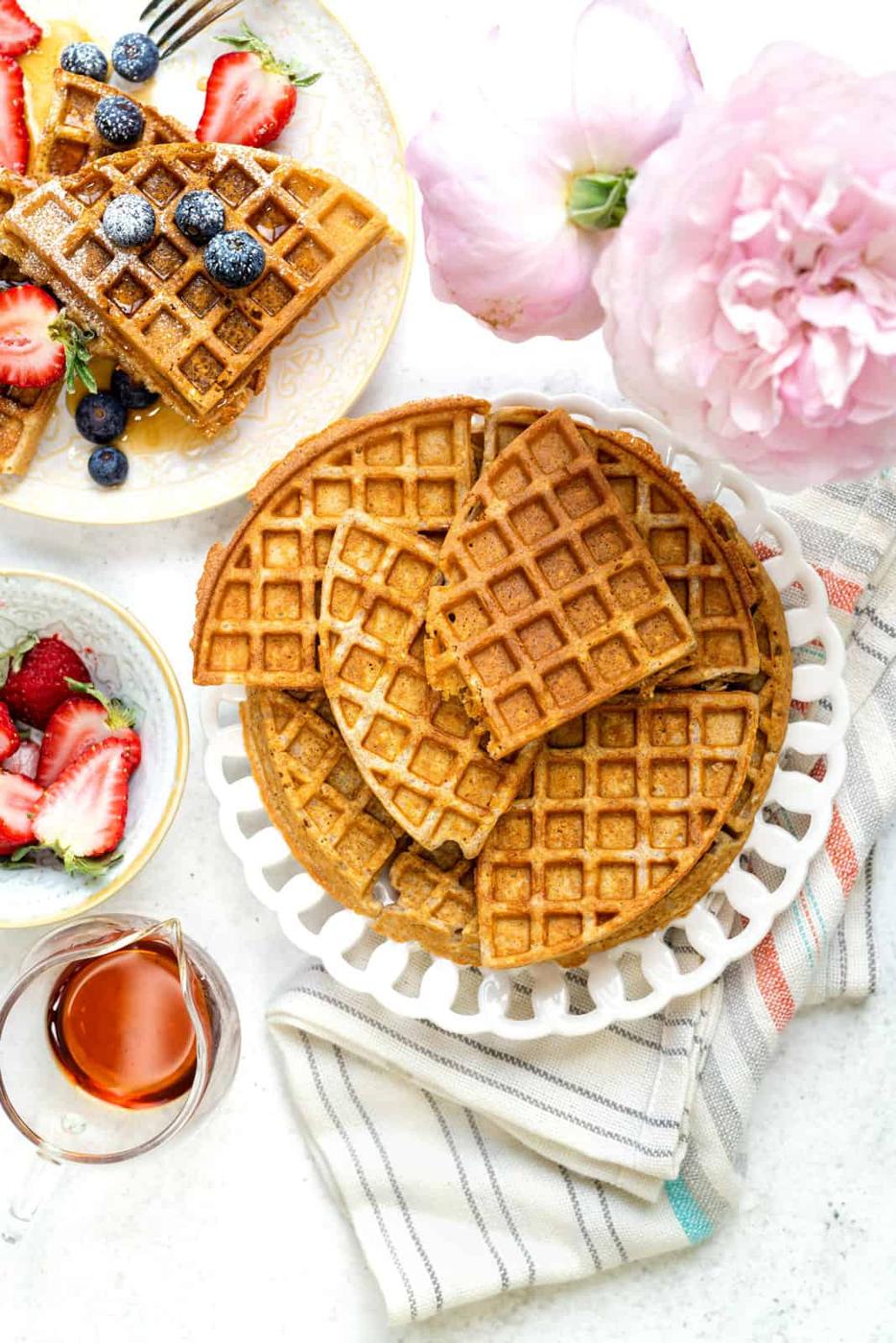 stack of oat waffles on a plate with serving of waffles and berries on the side
