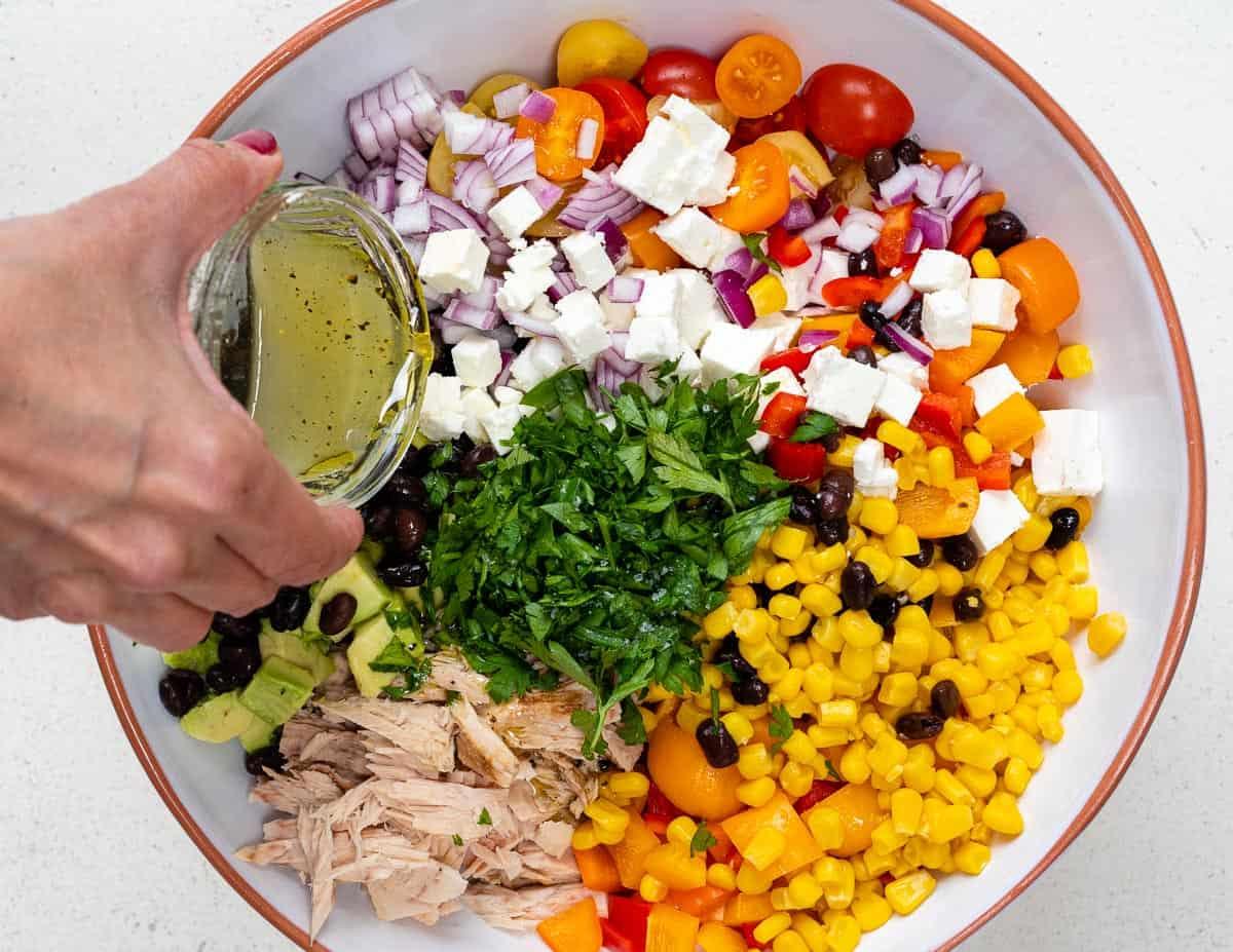 adding olive oil dressing to tuna pasta salad in a bowl