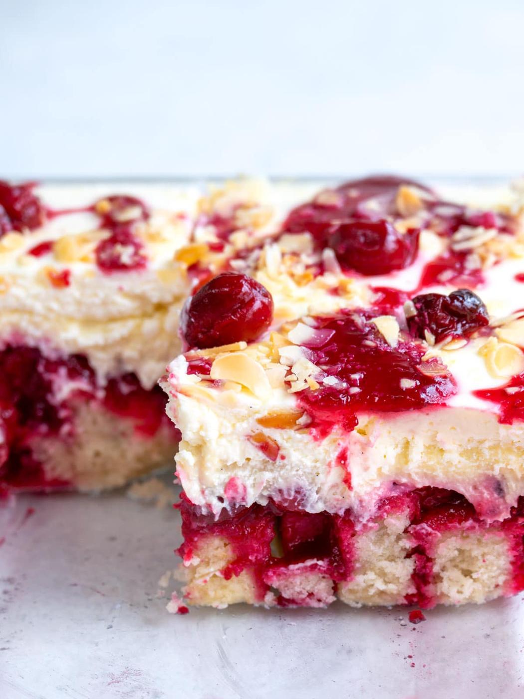A close-up of a Heaven On Earth cake with a slice removed, showing layers of white cake, creamy frosting, red cherries, and toasted almond slices on top.