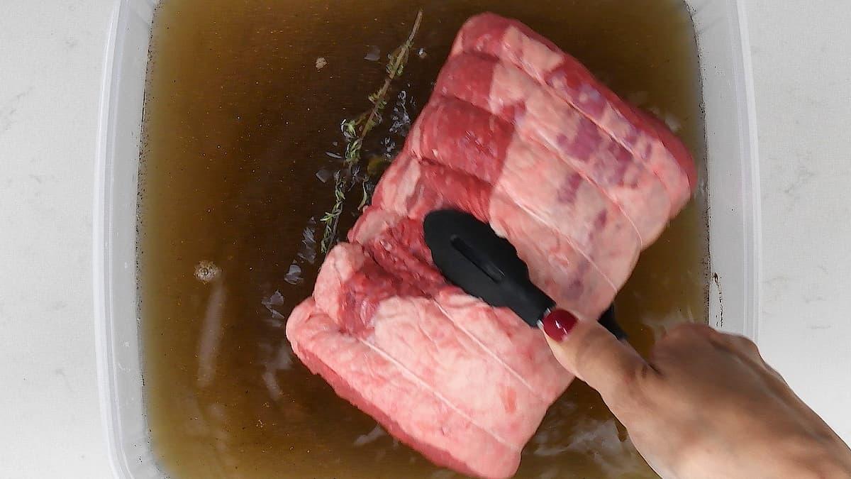 adding rolled brisket to container of brining solution