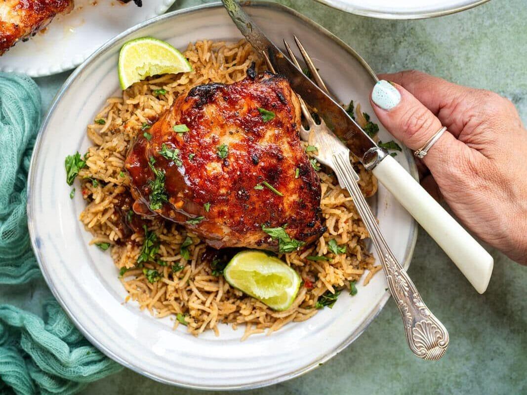 Vietnamese-style air fryer Honey Garlic Chicken Thighs served over rice in a bowl. Plates of chicken on the side.