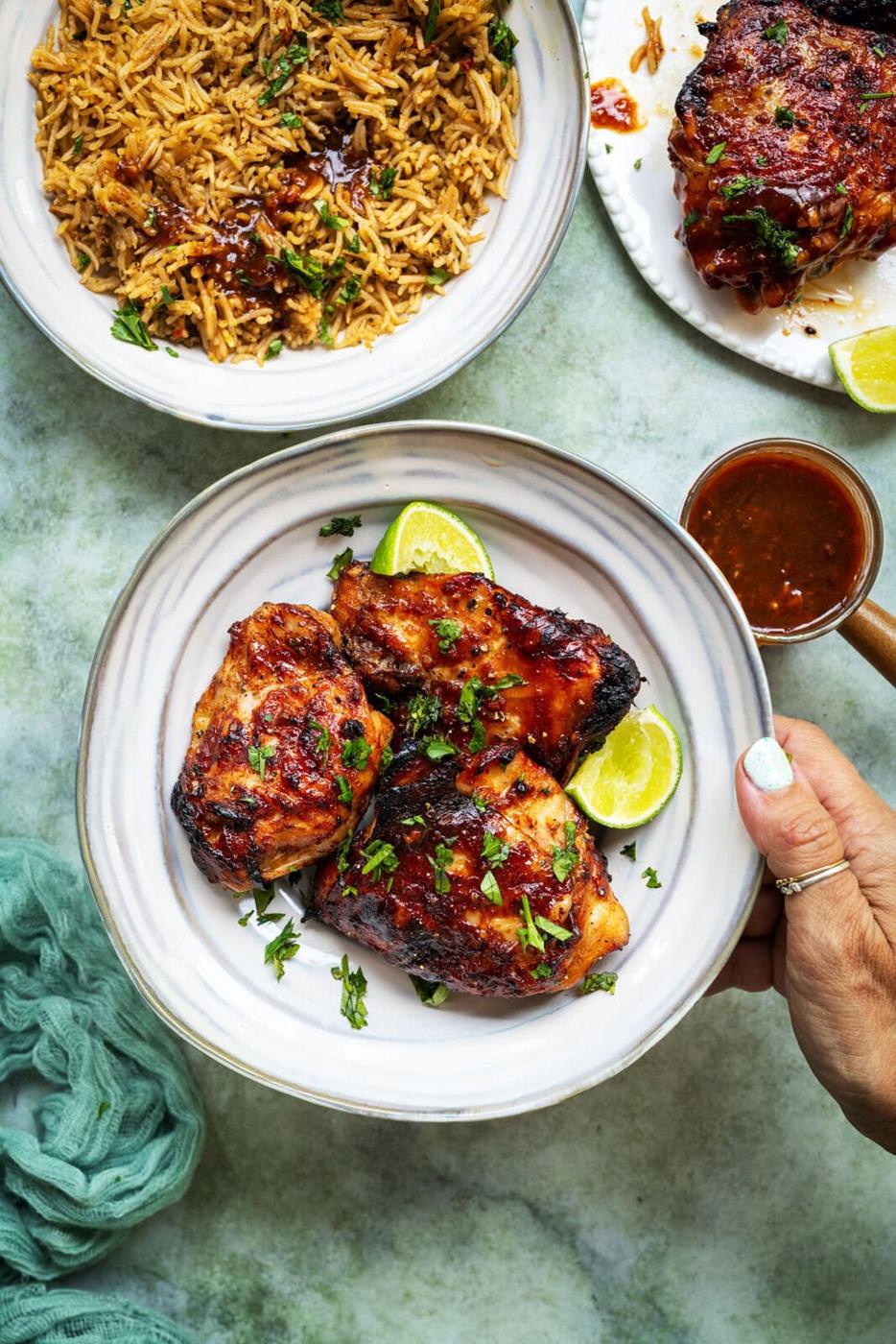 Air fryer honey garlic chicken thighs in a bowl, bowl of coconut rice and sticky sauce on the side