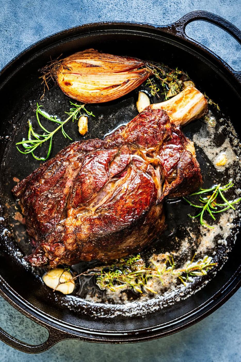 A seared bone-in ribeye steak (Cote de Boeuf) in a cast iron skillet with melted butter, garlic cloves, fresh rosemary, thyme, and a caramelized shallot.