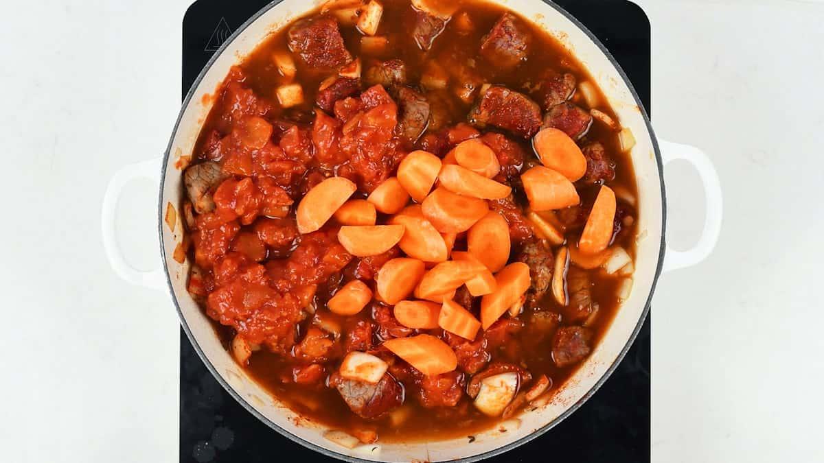 Adding carrots, chopped tomatoes and beef stock to the goulash