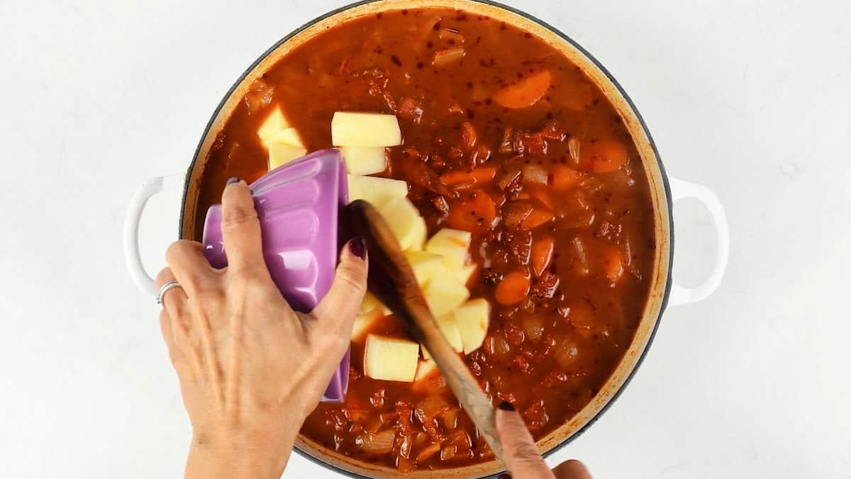 Stirring cubed potatoes into the simmering goulash