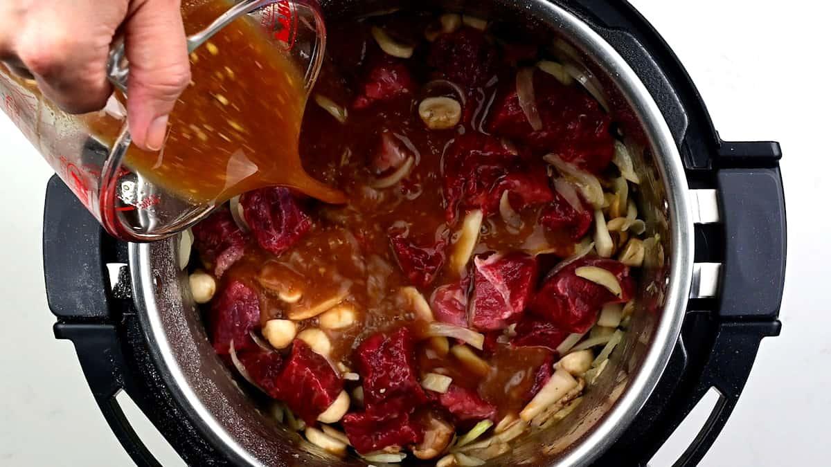 Adding beef broth to Instant Pot with cubed beef, mushrooms and onions