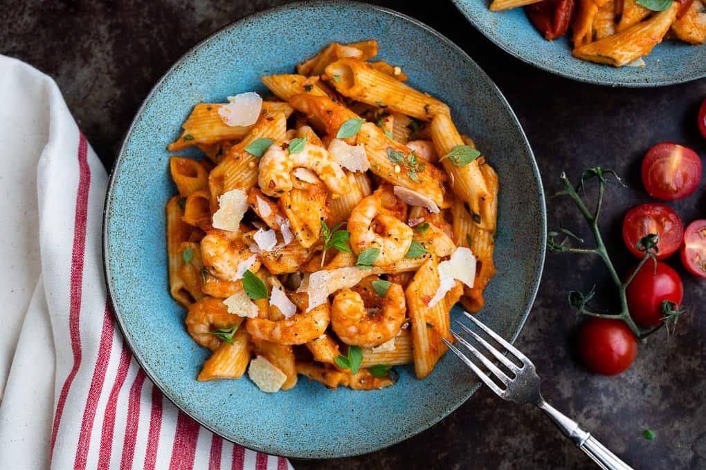 Bowl of shrimp penne all'arrabbiata with shaved cheese and basil leaves