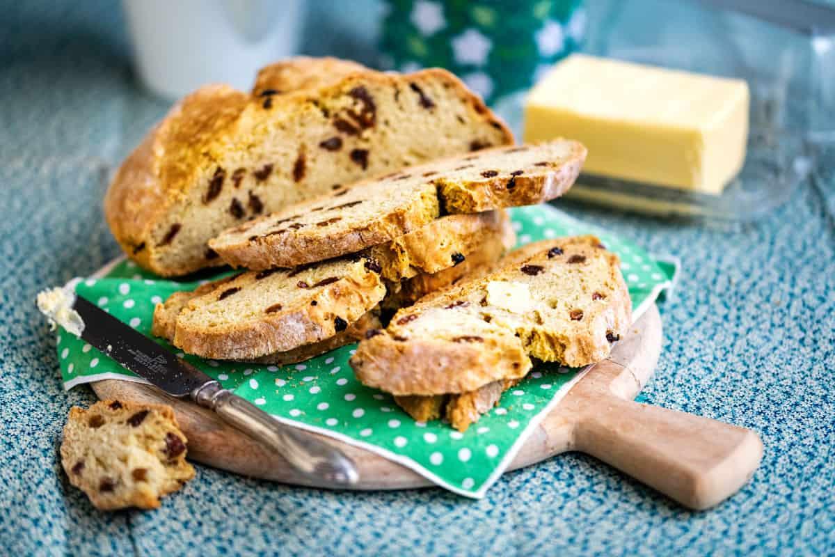 Vegan soda bread with raisins, sliced, on a wooden cutting board