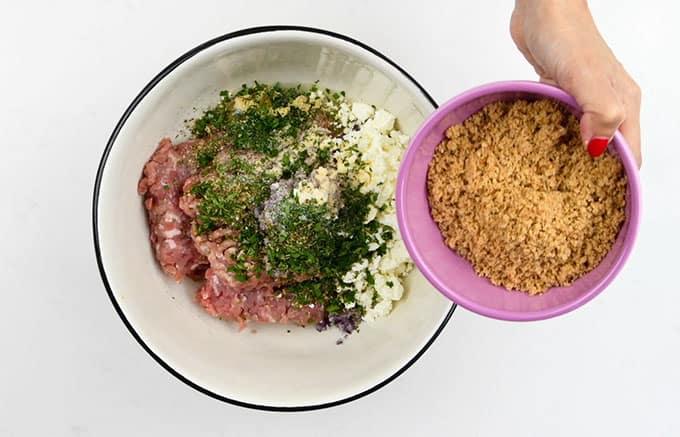 Adding ingredients for keftedes into a large bowl