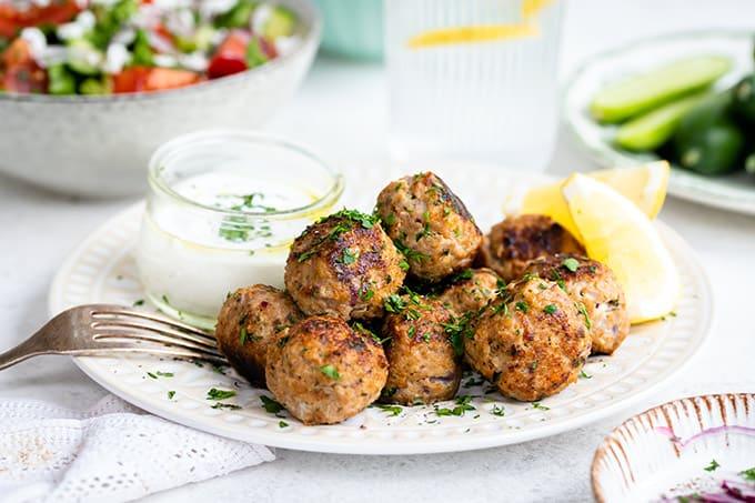 Close up on a plate of keftedes (Greek meatballs) with Greek salad in background