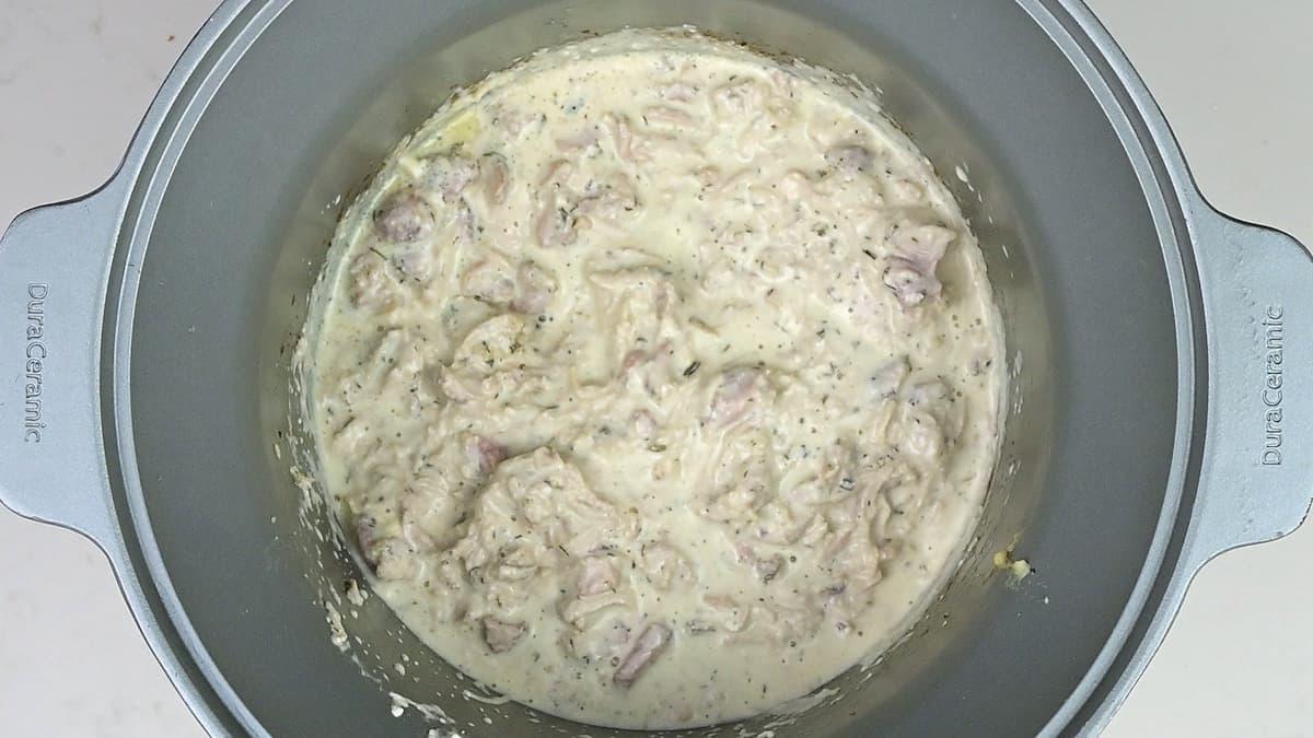 A pot filled with a creamy, thick mixture containing chunks of meat and herbs, possibly a keto-friendly stew or casserole, viewed from above. The dish appears to be in the cooking process, perhaps prepared in a slow cooker.