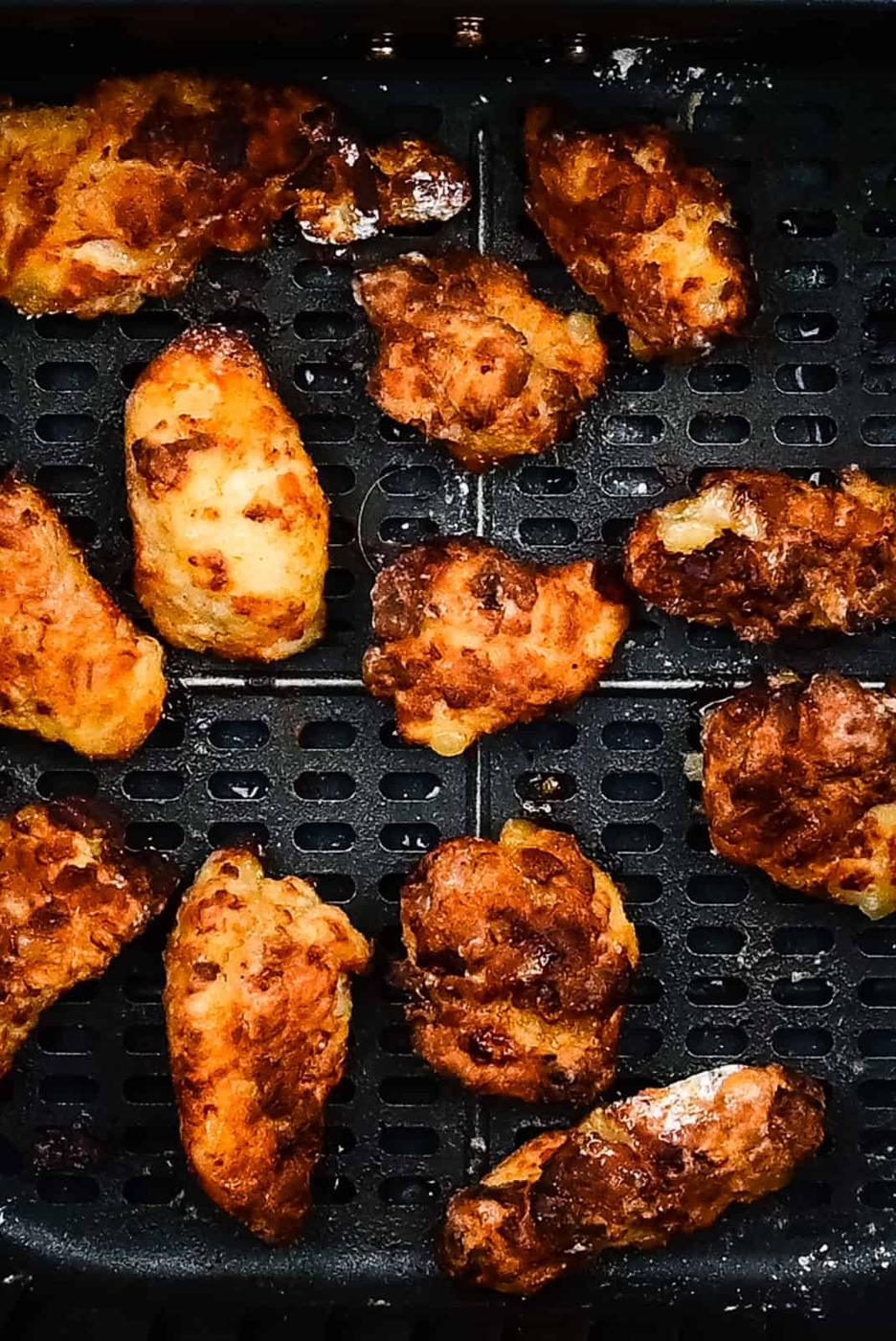 Golden brown, crispy Korean Fried Chicken wings are arranged in a single layer inside a black air fryer basket. The wings appear well-cooked with a crunchy coating.