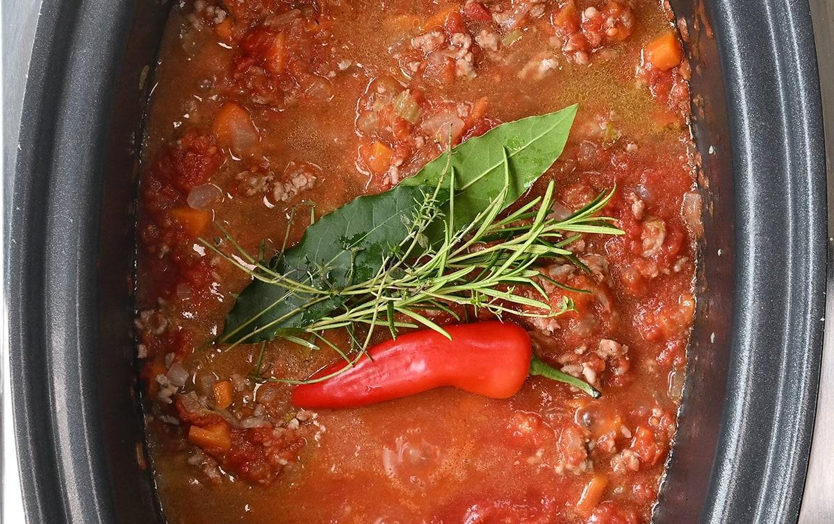 lamb ragu in a slow cooker, fresh herbs and chili on top