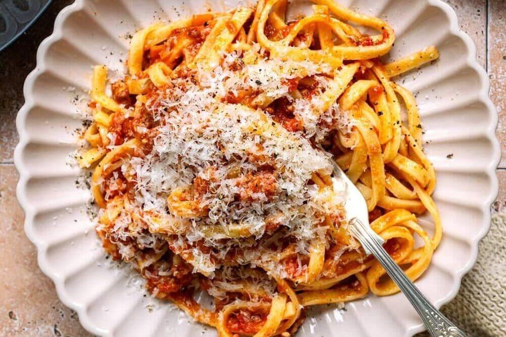 Serving of lamb ragu over paste in a bowl with grated cheese