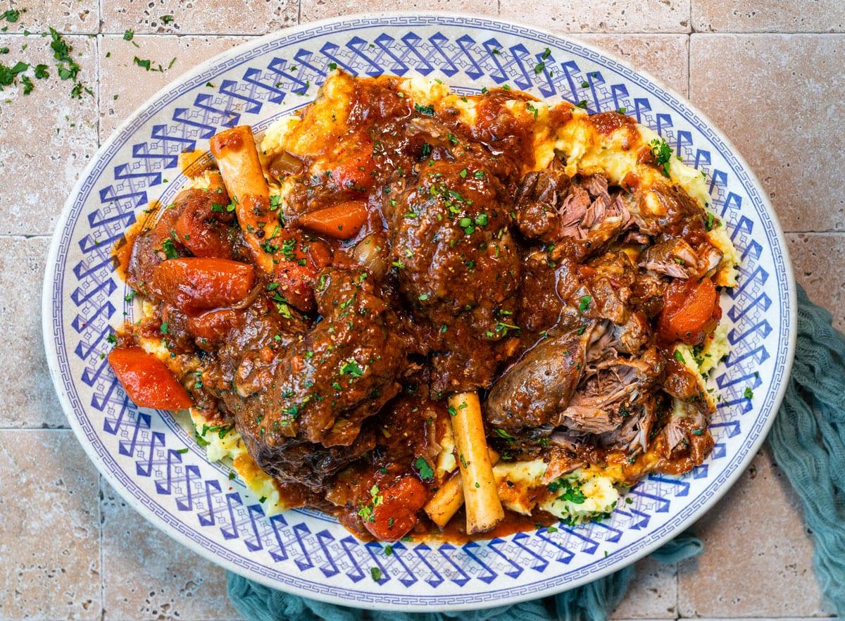 platter with braised lamb shanks in a red wine tomato sauce served over mashed potatoes