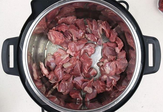 A top-down view of raw, chopped pieces of meat placed inside a stainless steel pot on a white surface, ready to become a comforting Lamb Tagine or slow cooker meal.