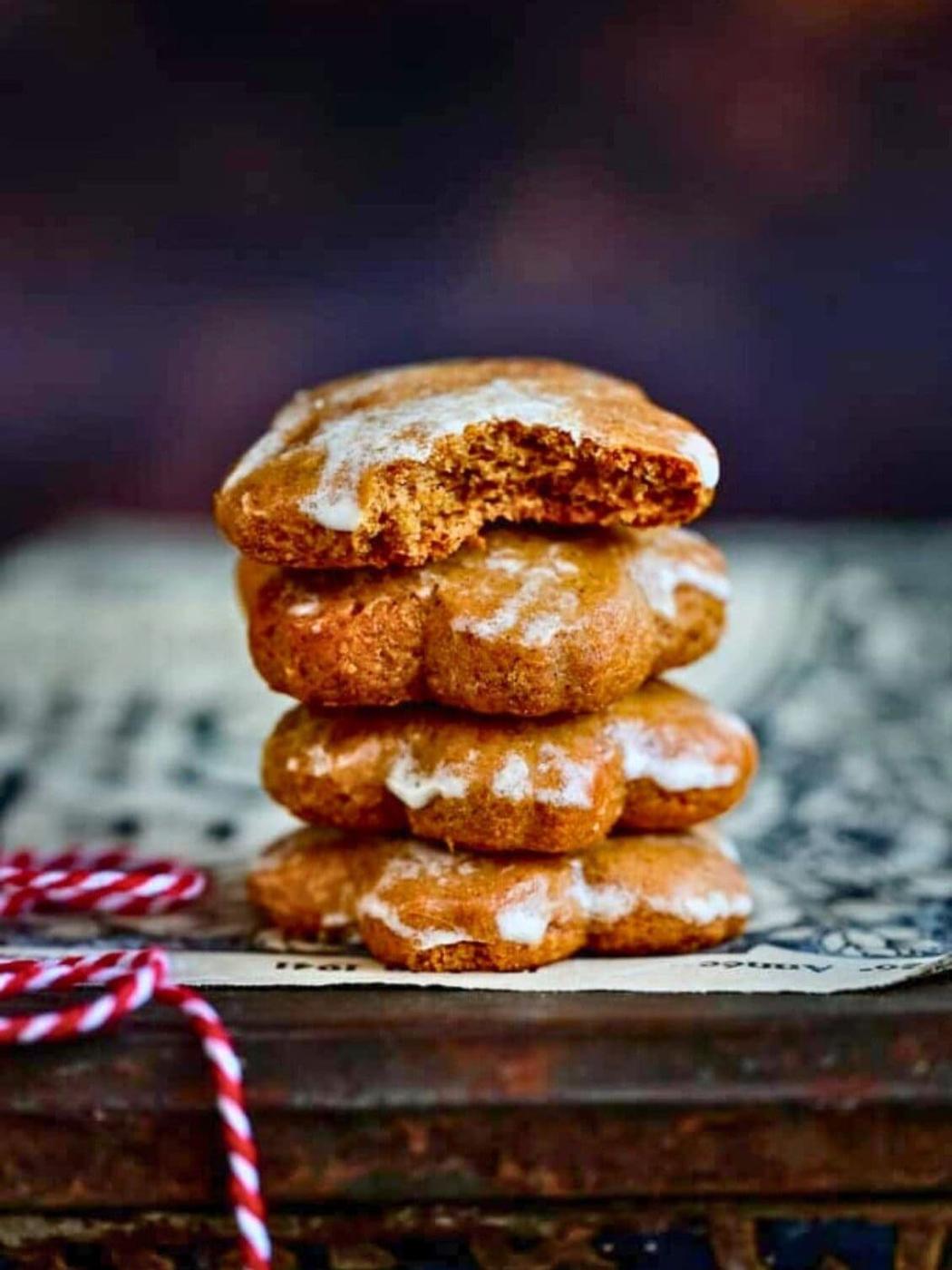 A stack of four Lebkuchen cookies with white icing, the top cookie has a bite taken out of it. The cookies rest on a piece of paper with a blurred dark background and a red-white string nearby.