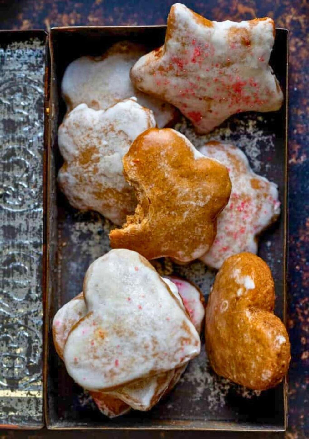 An overhead view of iced gingerbread Lebkuchen cookies in heart and star shapes, arranged in a rectangular metal tray. One heart-shaped lebkuchen cookie shows a bite taken out of it.