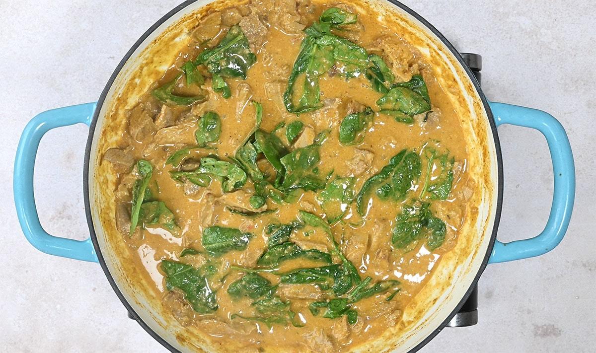 curry cooking in a skillet with spinach leaves