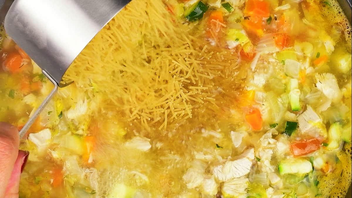 adding noodles to turkey soup cooking in a pot
