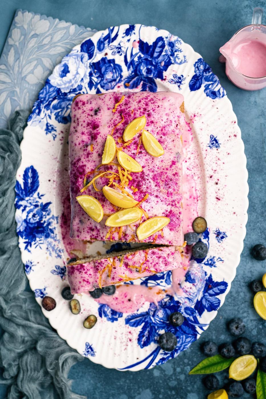Sliced lemon and blueberry loaf cake on a patterned platter against a blue background