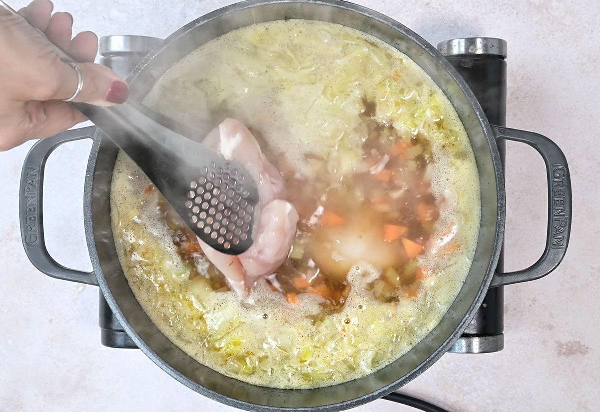 adding chicken breast to simmering broth to make soup