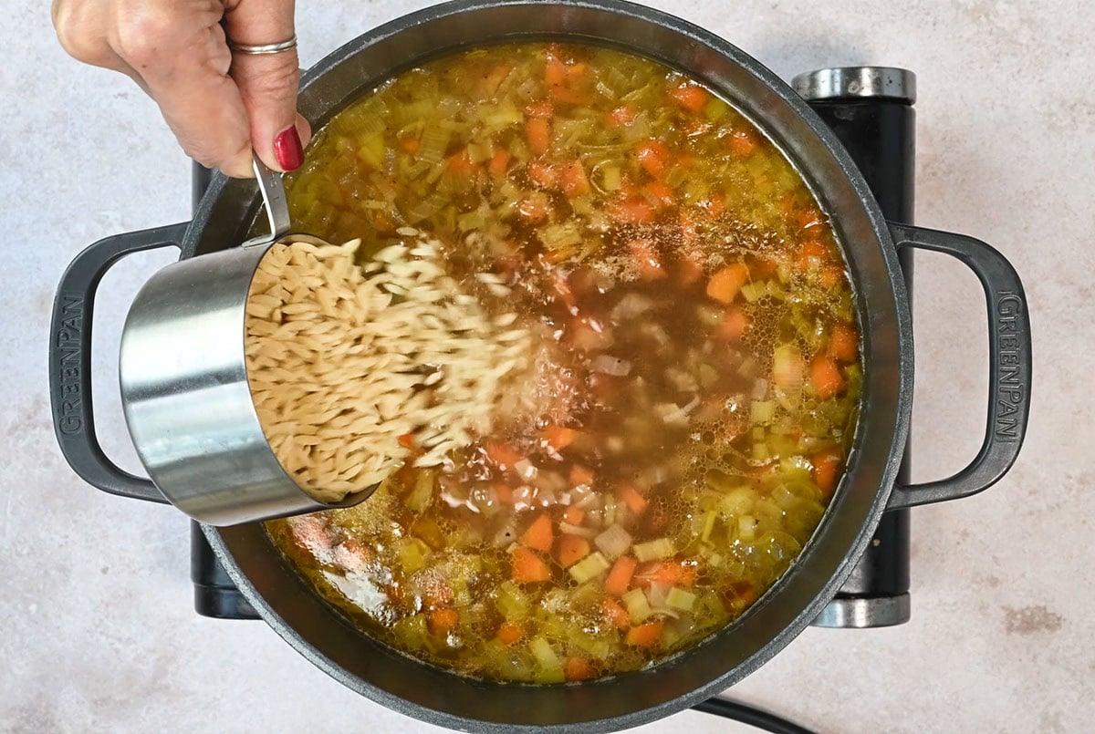adding orzo to a pot of simmering lemon chicken soup