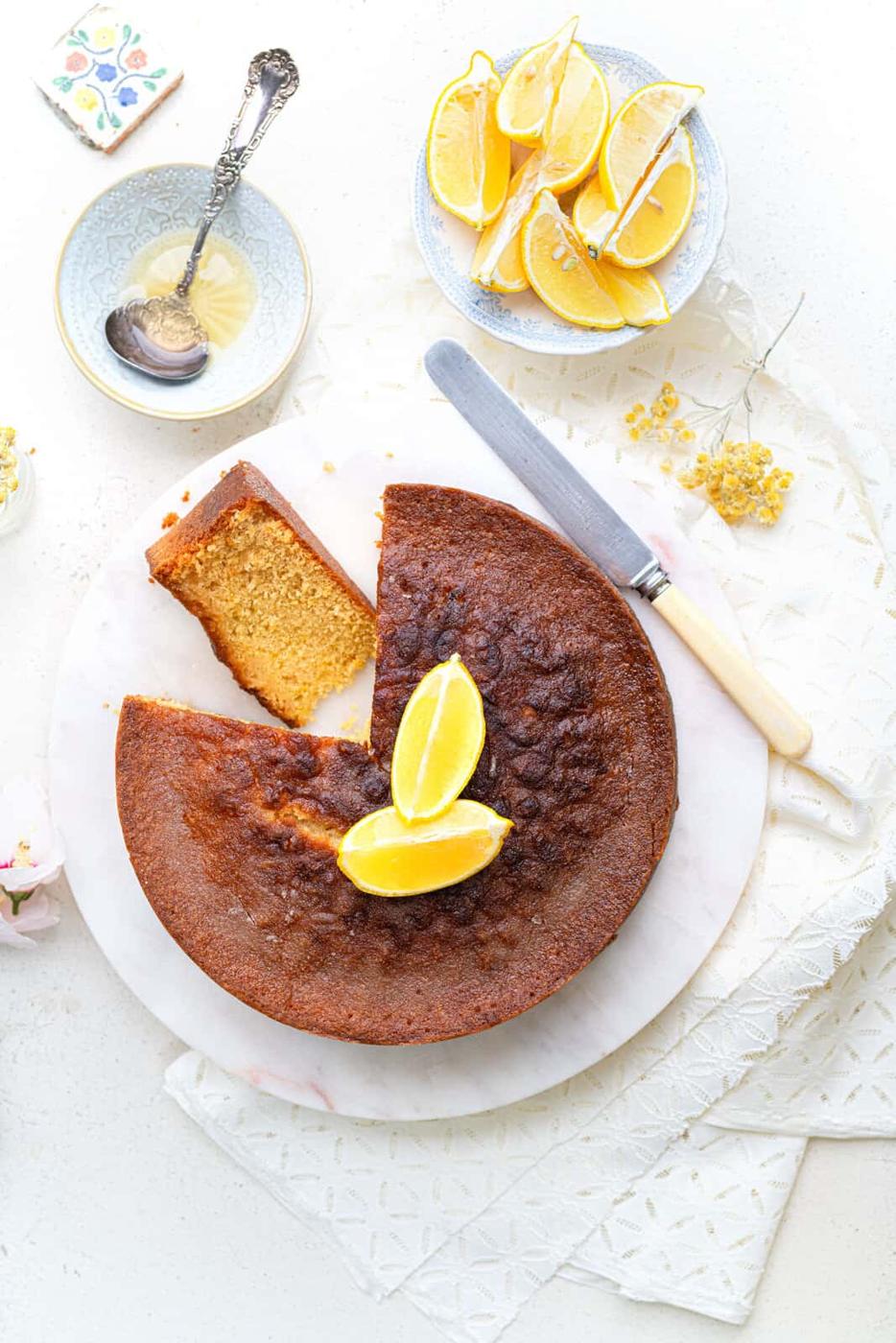 oveheard view of round lemon drizzle cake with slice cut out to show textrure of sponge